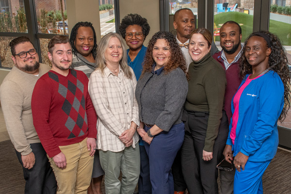 a diverse group of people pose and smile while standing in a hallway from baystate health’s diversity, equity and inclusion department