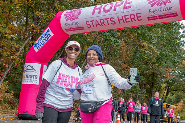 Two people stand under the pink arch at the Rays of Hope Walk & Run toward the Cure of Breast Cancer