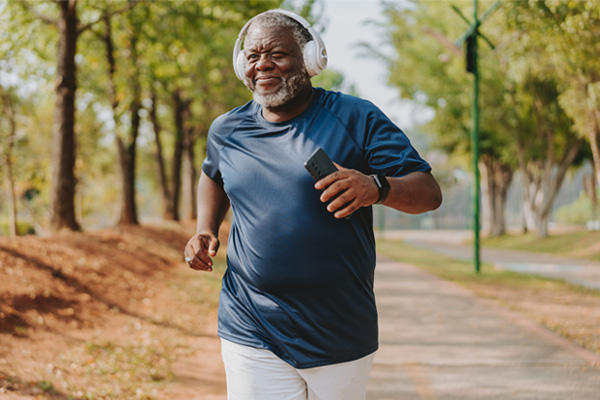 an older Black man jogging in a park, wearing headphones