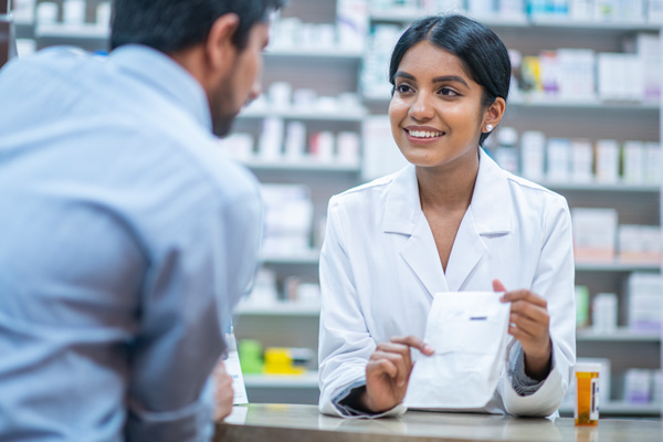 Woman pharmacist behind pharmacy counter, providing male patient with their medication.