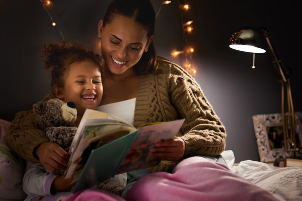 Woman caregiver reading book to smiling young girl.