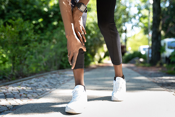 a woman's legs from the knees down, wearing athletic clothes and shoes, her hands on her calf in pain