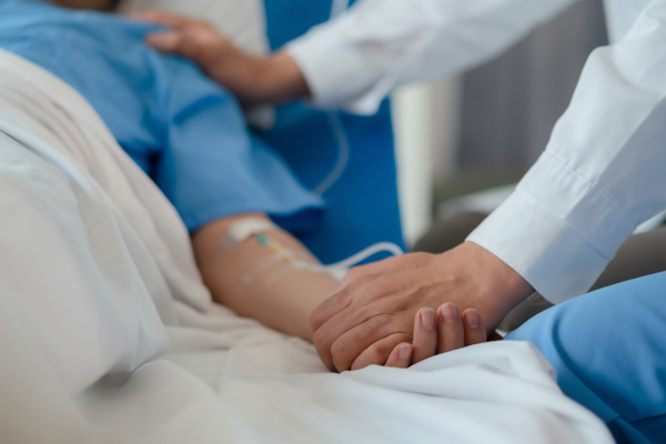 a patient in a hospital bed and a doctor by the bedside holding their hand