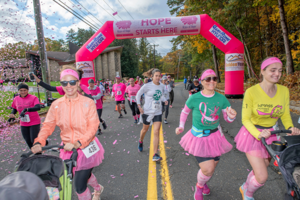 Runners run under a big pink arch at the 2023 Rays of Hope Walk & Run Toward the Cure of Breast Cancer.