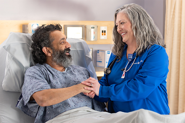 a caregiver and a patient in a hospital bed shaking hands and smiling