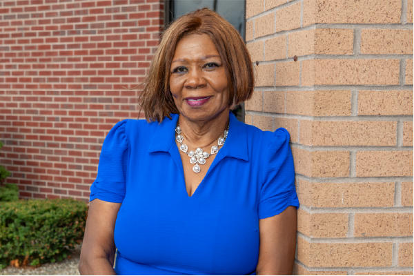 a woman of color, wearing a vibrant blue shirt, smiling for the camera