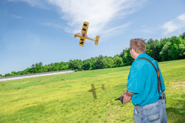 Man outside, flying a model airplane on a sunny day.