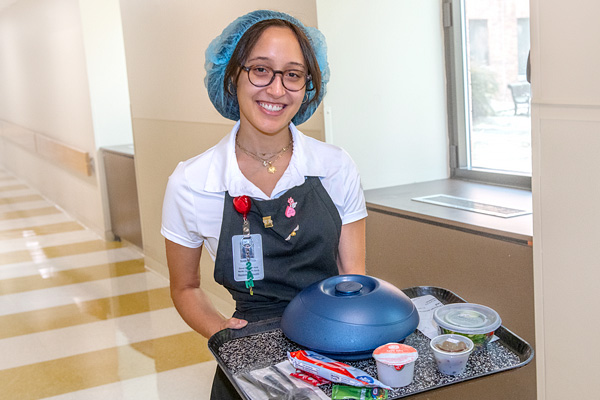 guest service employee smiling with a tray of hospital food