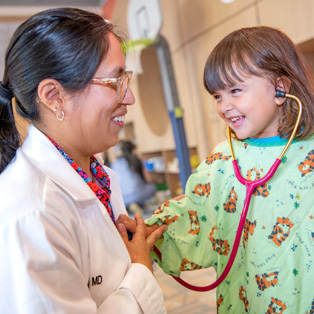 pediatric patient smiles as she places a stethoscope on a baystate children’s hospital provider’s heart